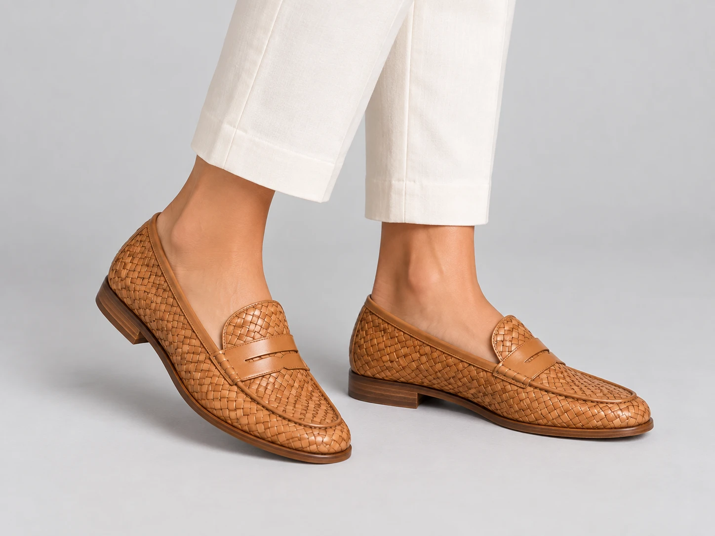 Pair of tan woven loafers photographed against a neutral studio backdrop